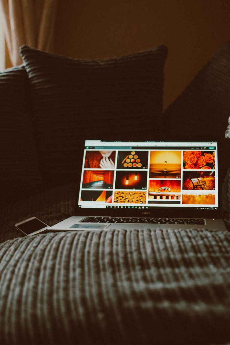 Laptop displaying photos surrounded by pillows, creating a cozy indoor environment.